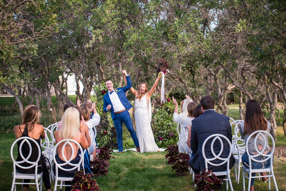 A bride and groom raise their arms in the air during their outdoor ceremony at The Oaks at Plum Creek.