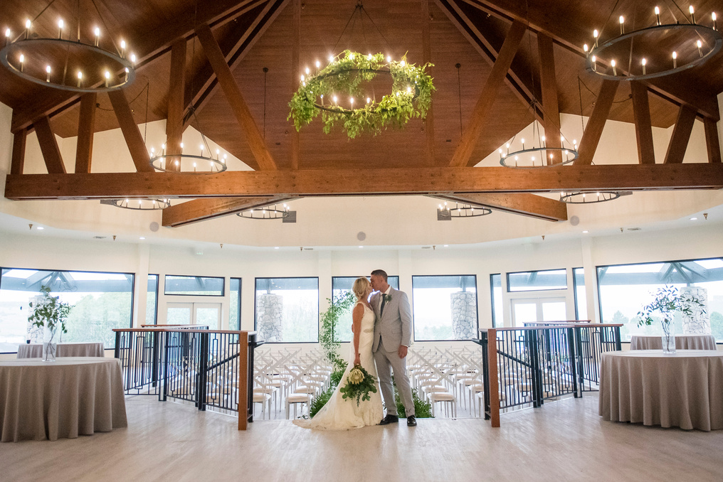 A bride and groom pose in front of a chandelier in the great room at The Oaks at Plum Creek.