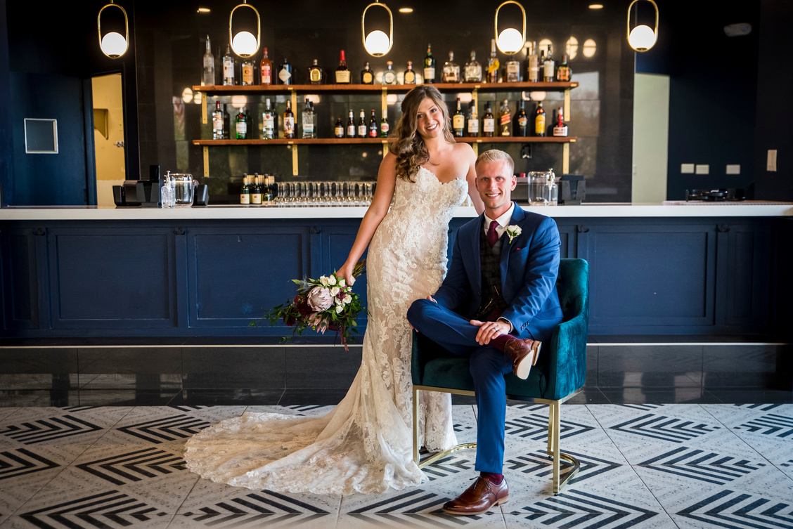 A wedding couple poses for a photo in front of the bar at The Oaks at Plum Creek in Denver, Colorado.