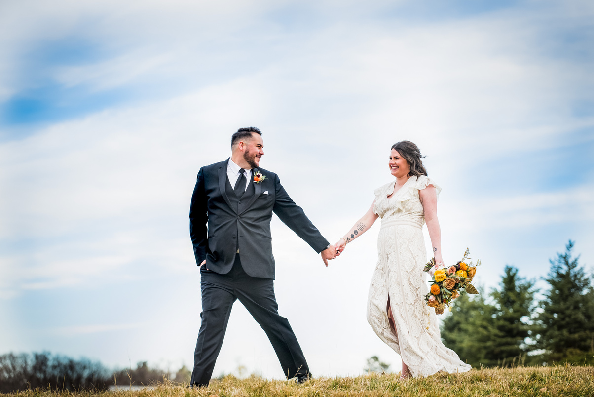 A bride and groom holding hands in a grassy field at The Oaks at Plum Creek in Castle Rock, Colorado.