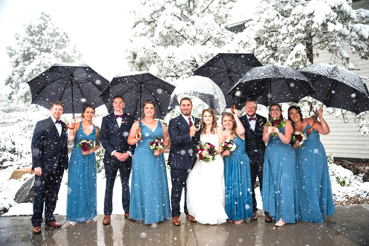 A group of bridesmaids and groomsmen with umbrellas in the snow.