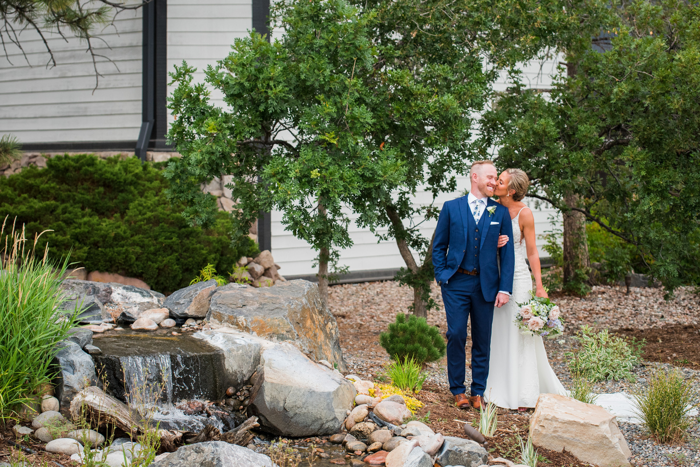 A bride and groom in front of a waterfall at their Denver wedding venue, The Oaks at Plum Creek.