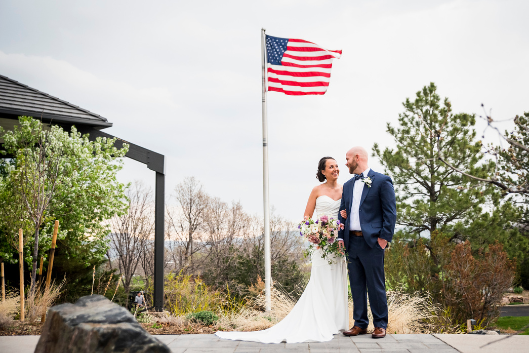 A bride and groom looking at each other in front of an American flag outside The Oaks at Plum Creek.
