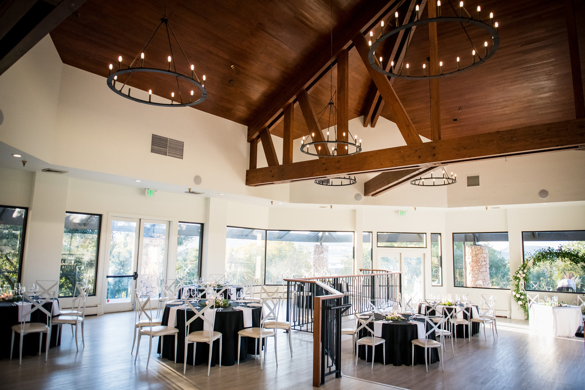 A wedding reception in a large room at The Oaks at Plum Creek with lots of tables and chandeliers.