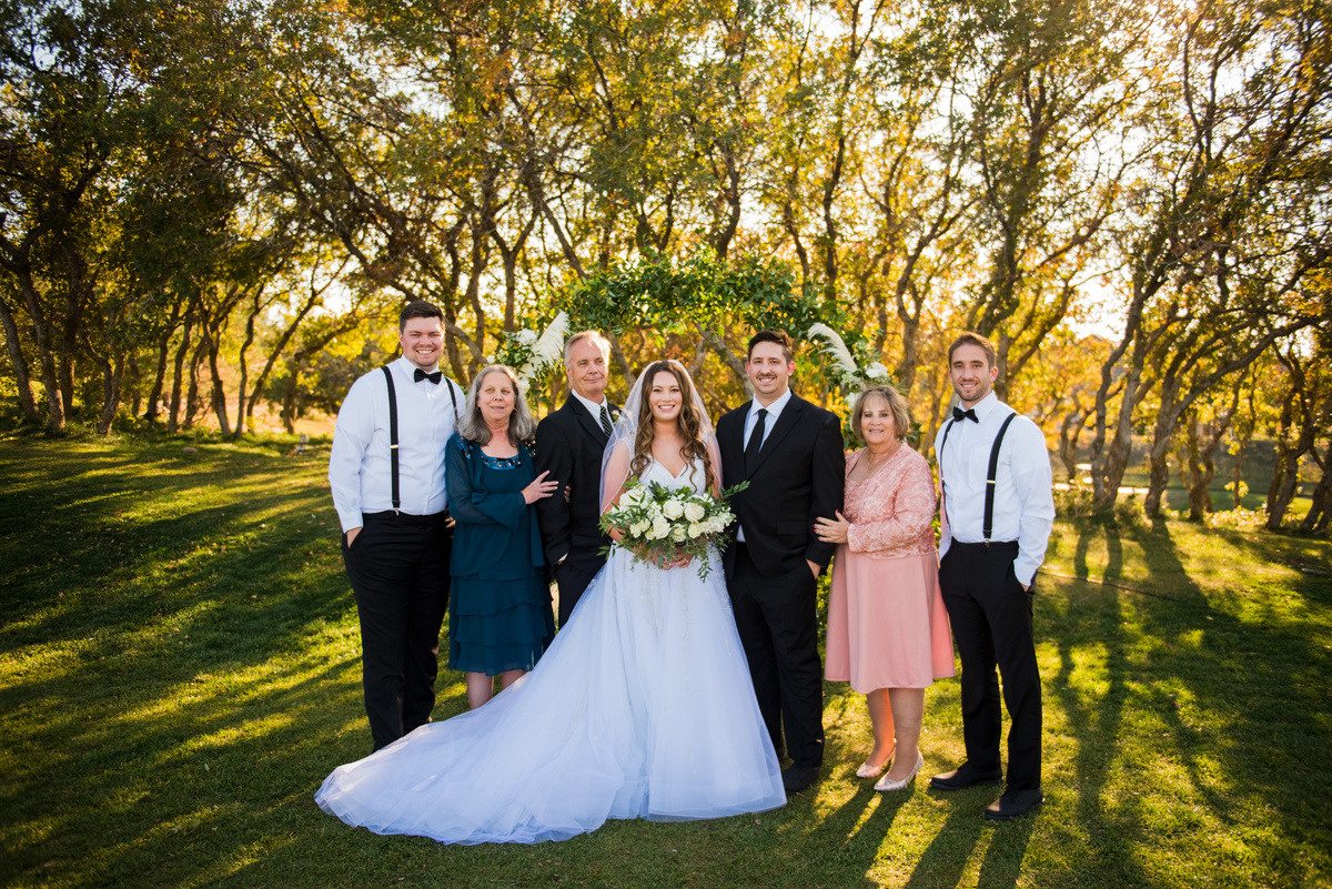 A wedding party poses for a photo in front of oak trees.