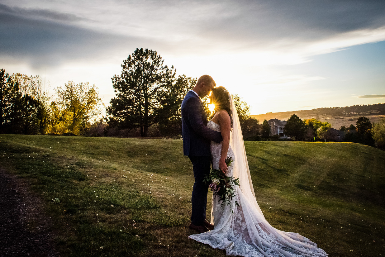 A bride and groom embrace with the sun setting behind them at The Oaks at Plum Creek in Denver, Colorado.
