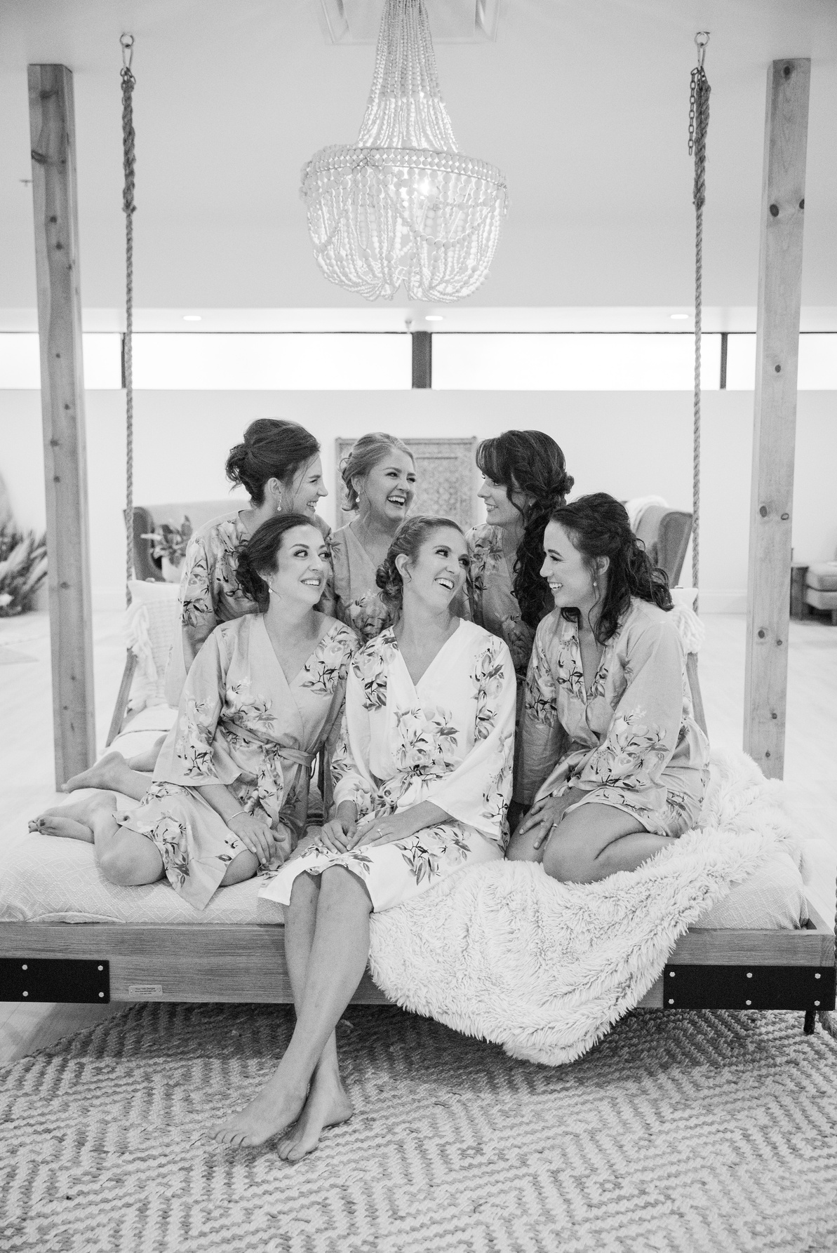 A black and white photo of bridesmaids sitting on the hanging bed in the getting ready space at The Oaks at Plum Creek in Castle Rock, Colorado.