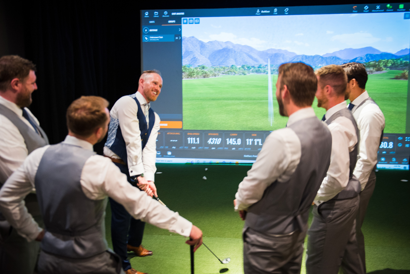 A group of groomsmen playing virtual golf on a large screen.